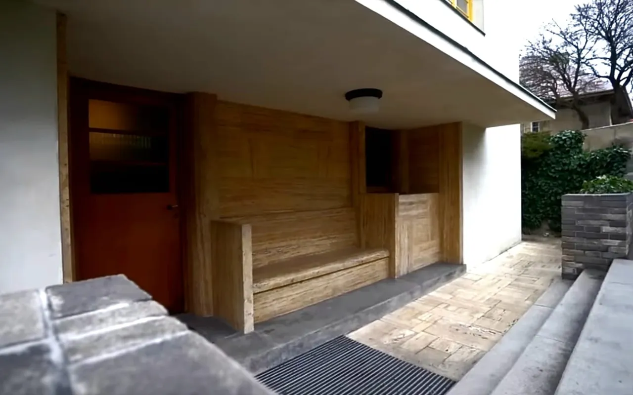 La nicchia d'ingresso di Villa Müller: una panchina in legno e una porta incassate nella parete bianca sotto il livello della strada